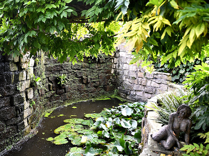 Beschutte kleine tuinvijver met waterlelies en stenen beeldje